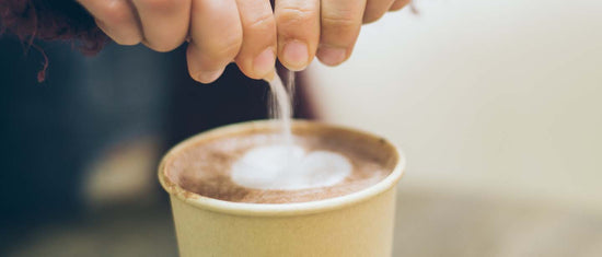 hands pouring an opened sugar packet into a cup of coffee